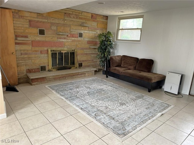 living room featuring a stone fireplace, wood walls, light tile patterned flooring, and a textured ceiling