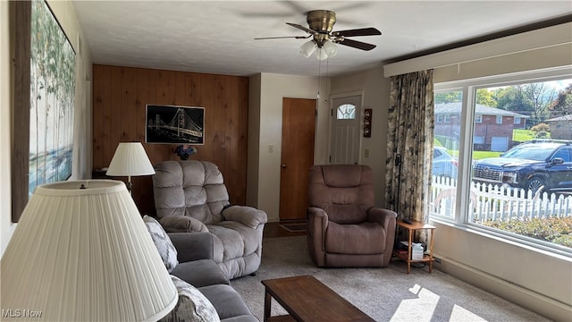 carpeted living room with ceiling fan and wood walls