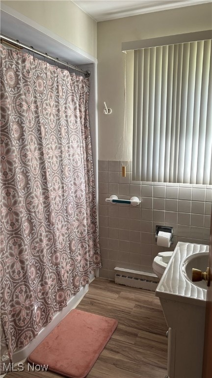 bathroom featuring hardwood / wood-style flooring, toilet, a baseboard radiator, vanity, and tile walls