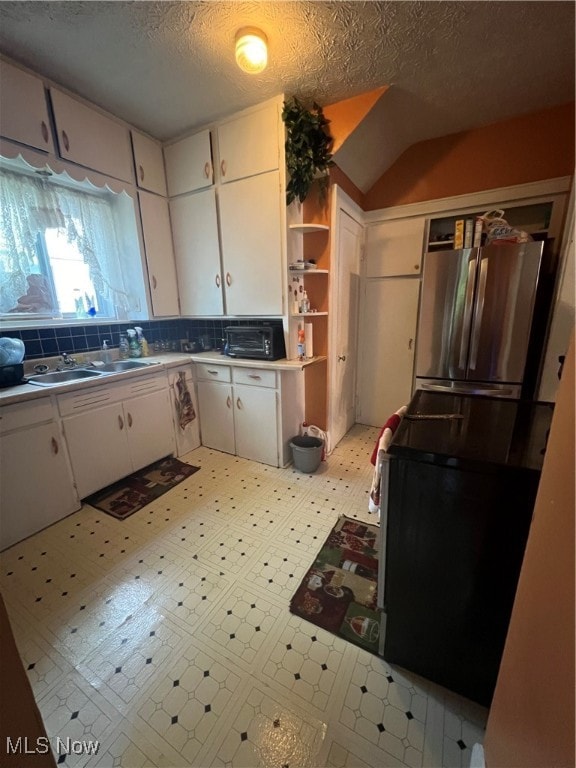 kitchen with a textured ceiling, stainless steel refrigerator, white cabinetry, and tasteful backsplash