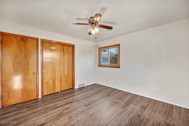 unfurnished bedroom with two closets, ceiling fan, and dark hardwood / wood-style floors