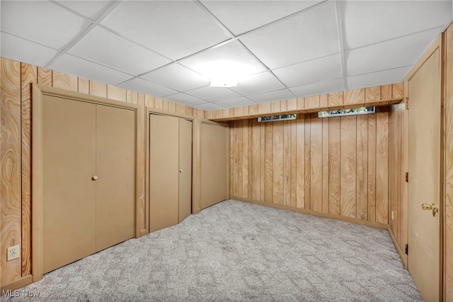 basement with a drop ceiling, wood walls, and light colored carpet