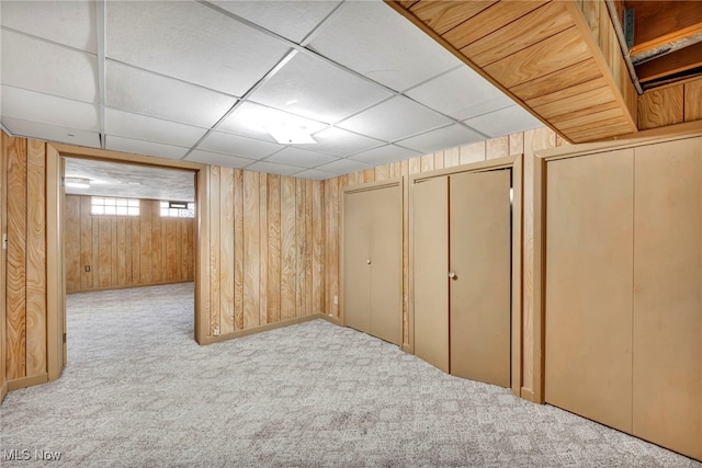 basement with light colored carpet, wood walls, and a paneled ceiling