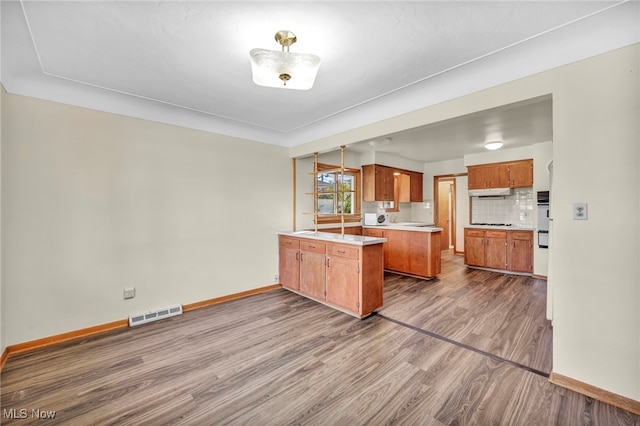 kitchen with tasteful backsplash, kitchen peninsula, a kitchen island, wood-type flooring, and cooktop