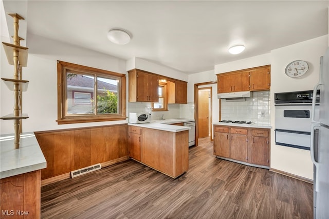 kitchen featuring dark hardwood / wood-style floors, sink, kitchen peninsula, decorative backsplash, and white appliances