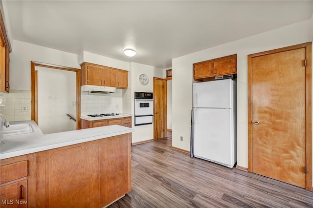 kitchen with sink, light hardwood / wood-style floors, white appliances, and decorative backsplash