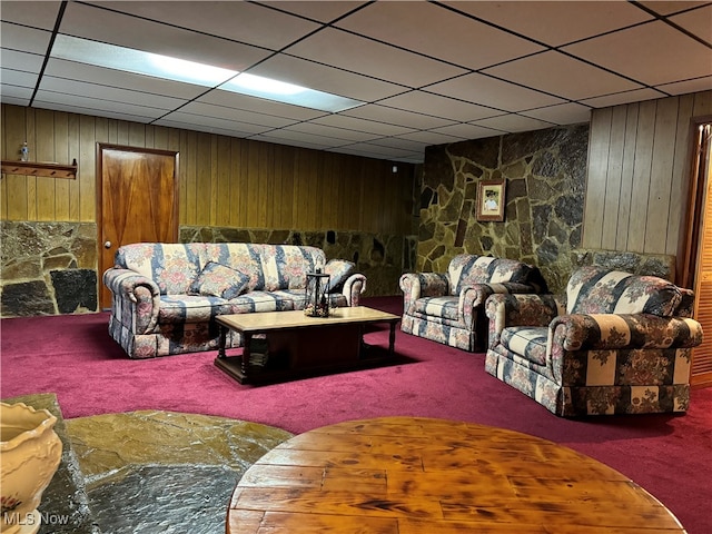 carpeted living room featuring a drop ceiling and wood walls