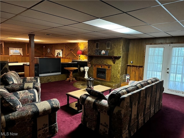 living room featuring a drop ceiling, wooden walls, dark colored carpet, and a fireplace