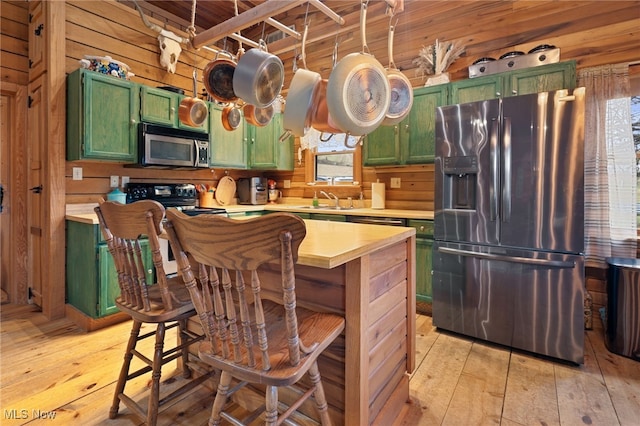 kitchen featuring wood walls, sink, stainless steel appliances, green cabinets, and light wood-type flooring