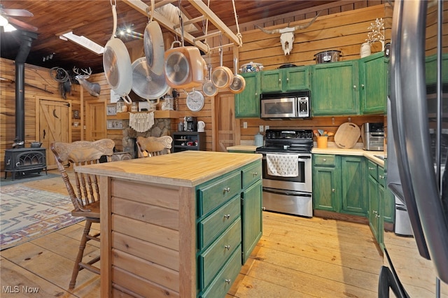 kitchen with wood walls, a wood stove, green cabinetry, and stainless steel appliances