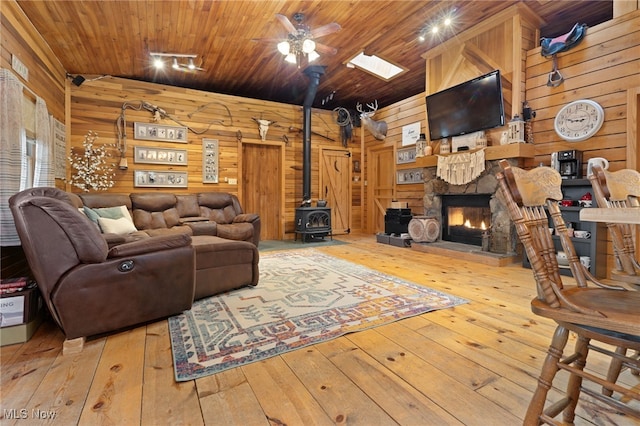 living room featuring ceiling fan, wood ceiling, wood walls, a stone fireplace, and light wood-type flooring