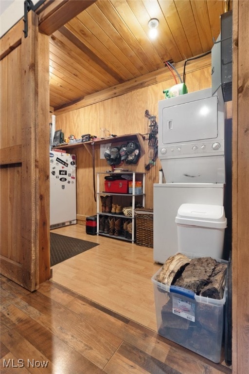 washroom with wood ceiling, a barn door, stacked washer and clothes dryer, wood walls, and hardwood / wood-style floors