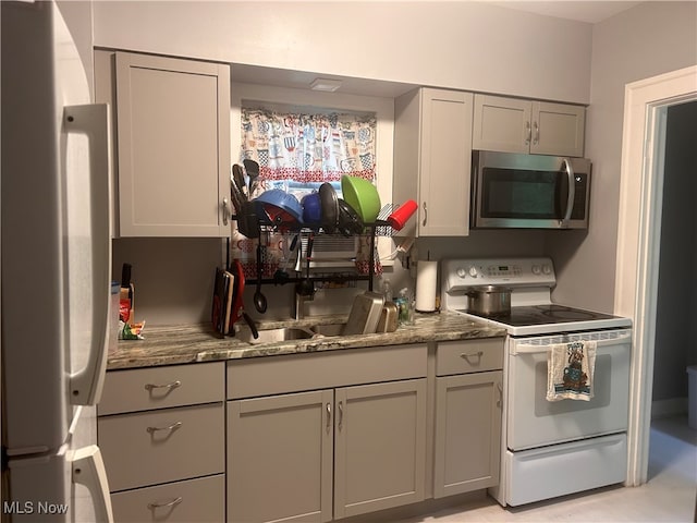 kitchen with gray cabinetry, white appliances, and dark stone countertops