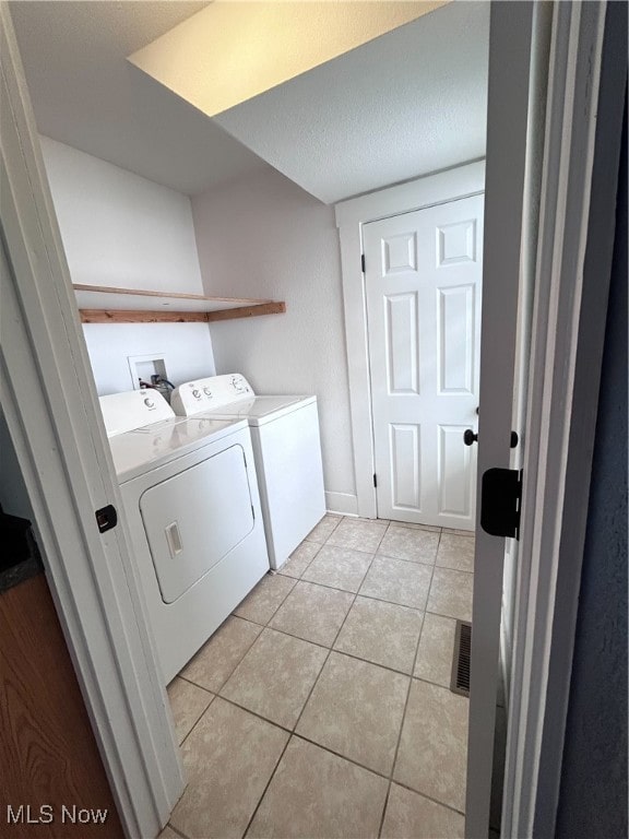 laundry room with a textured ceiling, light tile patterned floors, and washing machine and clothes dryer