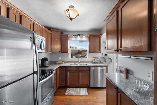 kitchen with sink, stone countertops, a textured ceiling, stainless steel appliances, and dark hardwood / wood-style flooring