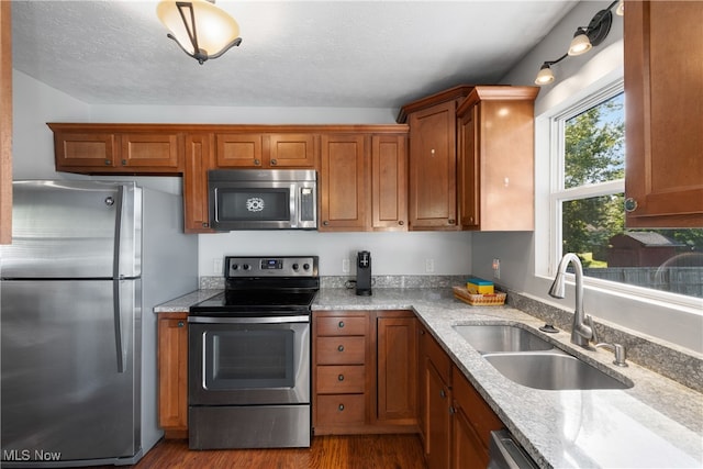 kitchen with light stone counters, sink, a textured ceiling, hardwood / wood-style flooring, and stainless steel appliances