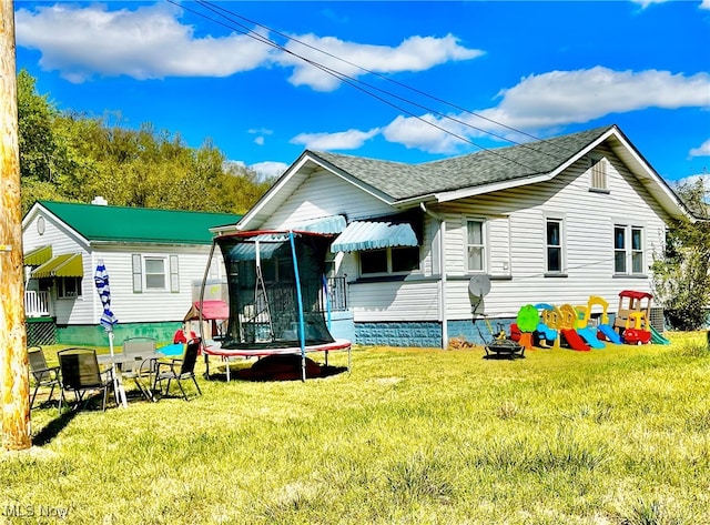 back of property with a trampoline and a yard