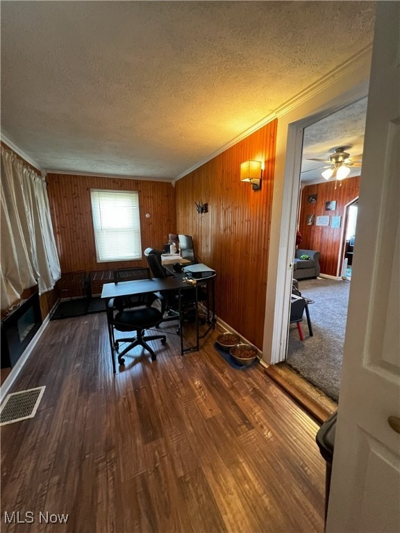 home office featuring dark hardwood / wood-style flooring, a textured ceiling, wooden walls, crown molding, and ceiling fan