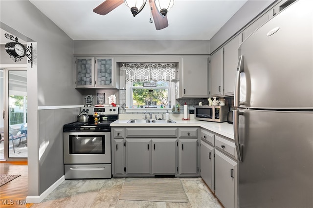 kitchen featuring gray cabinets, sink, decorative backsplash, stainless steel appliances, and ceiling fan