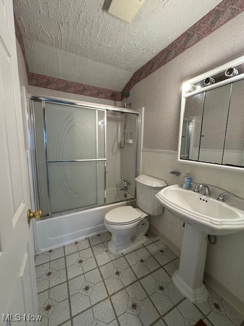 bathroom with toilet, combined bath / shower with glass door, and a textured ceiling