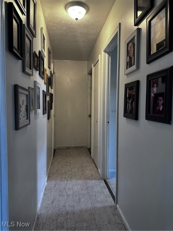 corridor featuring a textured ceiling and light hardwood / wood-style floors