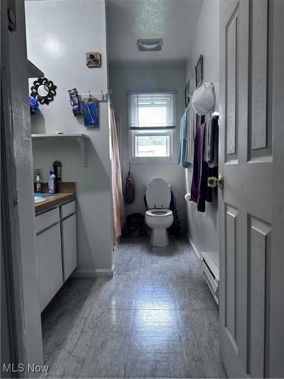 bathroom featuring a baseboard heating unit, a textured ceiling, toilet, vanity, and curtained shower