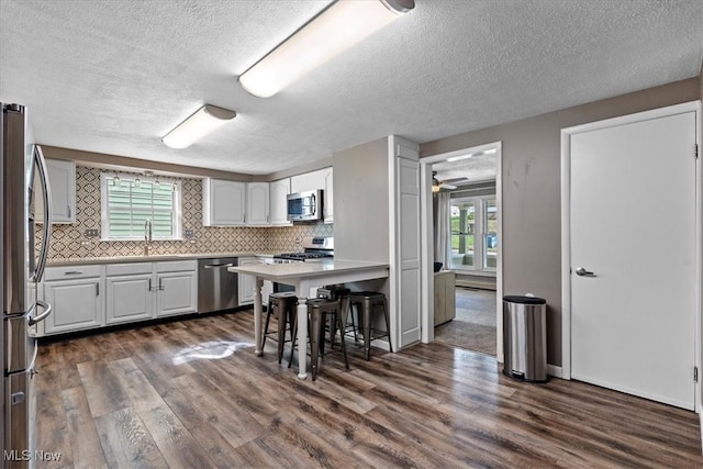 kitchen with a breakfast bar, a wealth of natural light, appliances with stainless steel finishes, and dark wood-type flooring