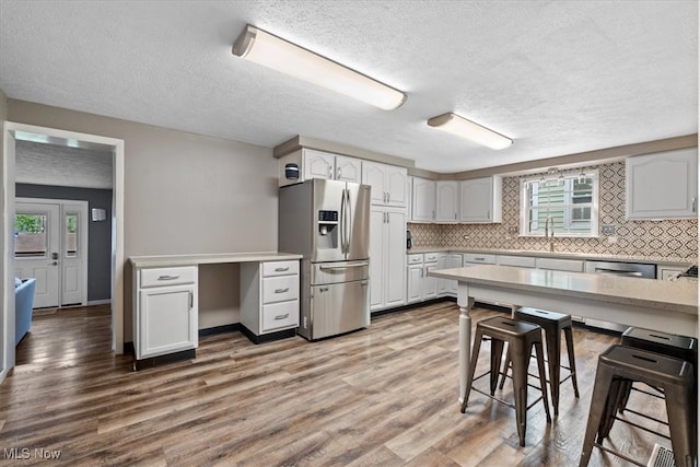 kitchen with white cabinets, light hardwood / wood-style floors, appliances with stainless steel finishes, and a textured ceiling