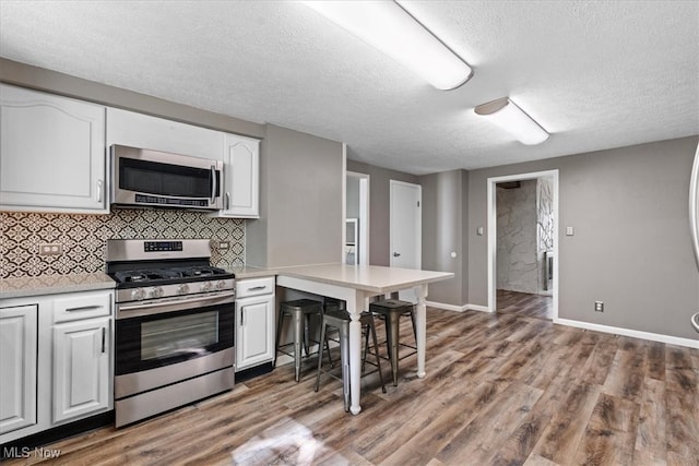 kitchen with decorative backsplash, white cabinetry, stainless steel appliances, a textured ceiling, and light hardwood / wood-style flooring