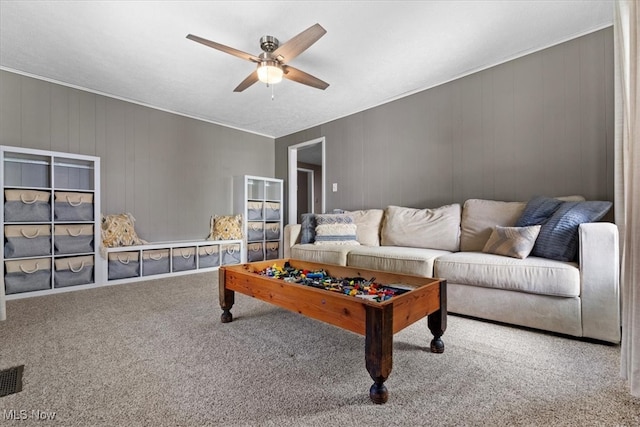 carpeted living room featuring wooden walls and ceiling fan