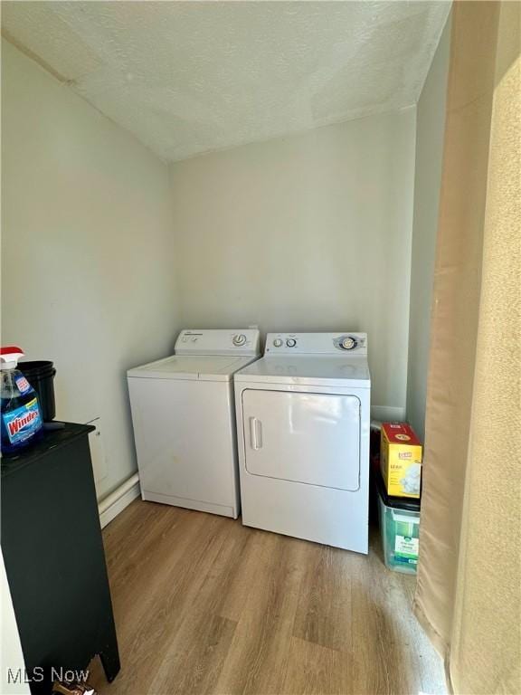 clothes washing area featuring washing machine and dryer, light hardwood / wood-style floors, and a textured ceiling