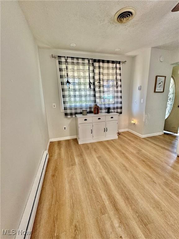 spare room featuring a baseboard heating unit, a textured ceiling, and light hardwood / wood-style floors