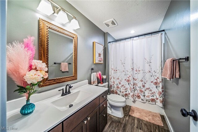 full bathroom with shower / bath combination with curtain, a textured ceiling, hardwood / wood-style flooring, vanity, and toilet