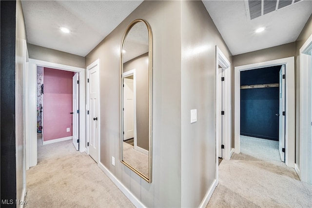 hall featuring a textured ceiling and light colored carpet