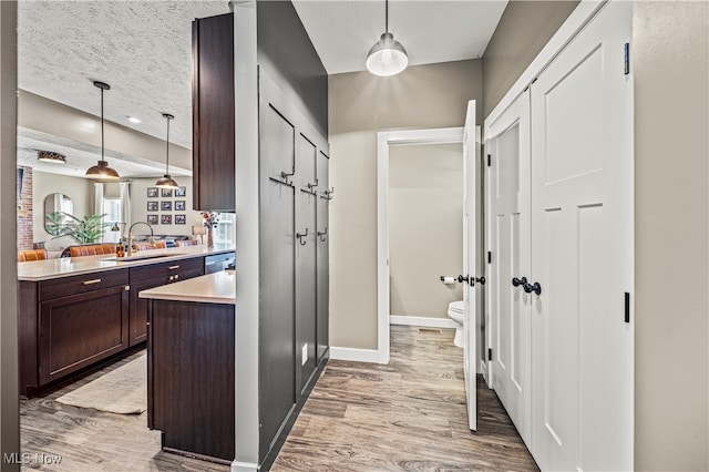 kitchen with dark brown cabinetry, sink, a textured ceiling, decorative light fixtures, and light hardwood / wood-style flooring