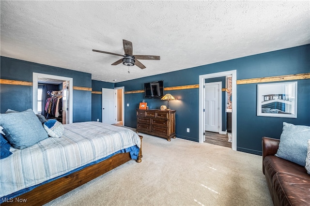 carpeted bedroom with a textured ceiling, ceiling fan, and a walk in closet