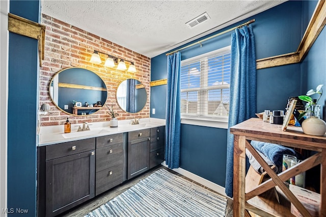 bathroom with a textured ceiling, vanity, and brick wall