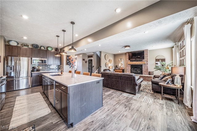 kitchen featuring appliances with stainless steel finishes, a textured ceiling, dark brown cabinetry, light hardwood / wood-style flooring, and a center island with sink