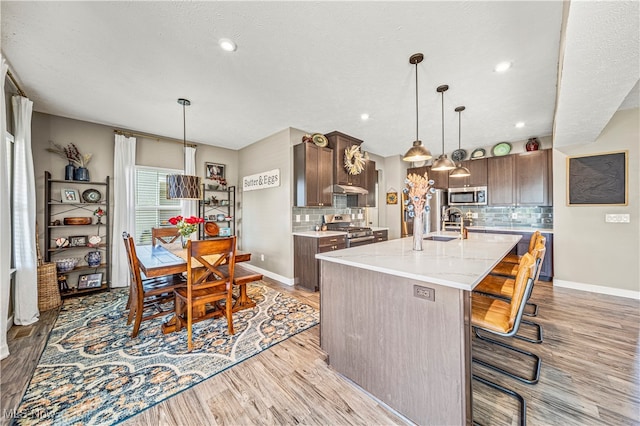 kitchen featuring an island with sink, appliances with stainless steel finishes, decorative backsplash, and light hardwood / wood-style flooring