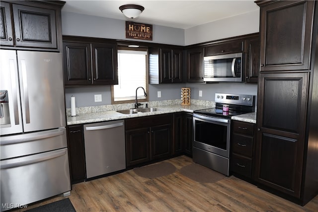 kitchen featuring light stone counters, dark brown cabinetry, stainless steel appliances, sink, and dark hardwood / wood-style floors