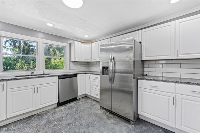 kitchen with appliances with stainless steel finishes, decorative backsplash, white cabinetry, dark stone counters, and sink