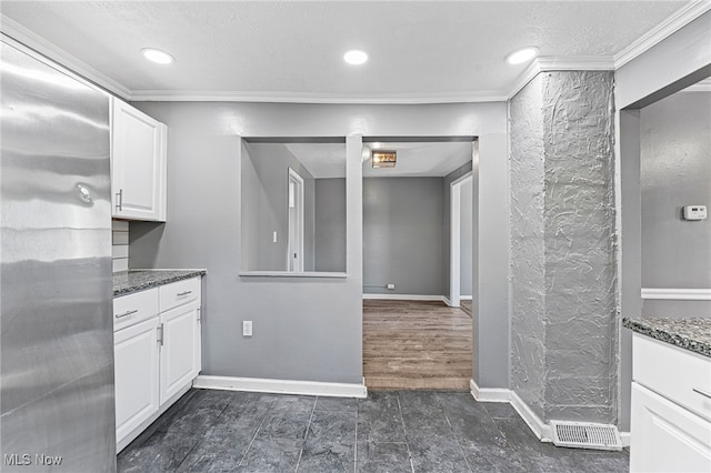 kitchen featuring dark hardwood / wood-style floors, white cabinets, stainless steel refrigerator, crown molding, and dark stone countertops