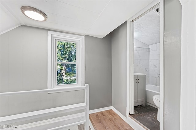 bathroom with tiled shower / bath combo, vaulted ceiling, hardwood / wood-style floors, and toilet