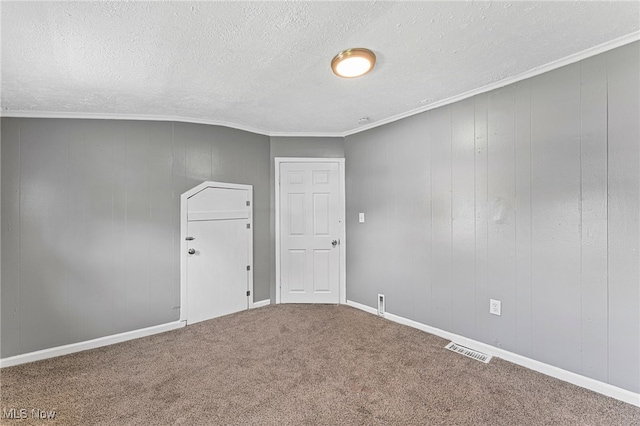 empty room with ornamental molding, carpet, a textured ceiling, and wood walls