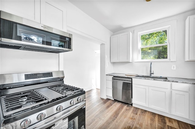 kitchen featuring light wood-type flooring, sink, white cabinets, appliances with stainless steel finishes, and dark stone countertops