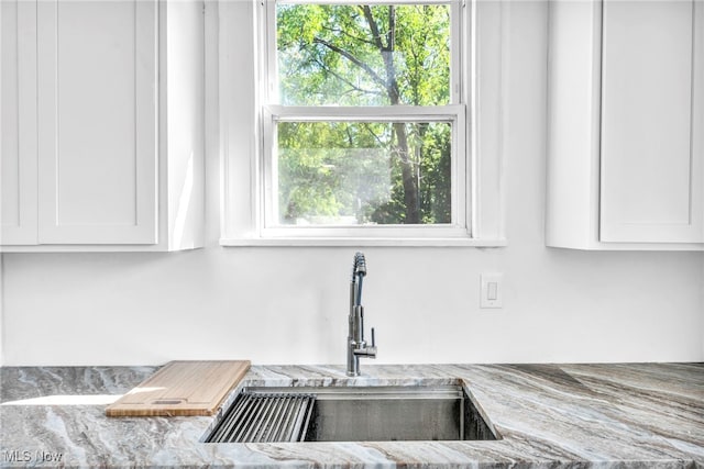 interior details featuring light stone countertops, white cabinetry, and sink