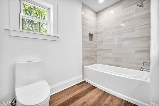 bathroom with wood-type flooring, tiled shower / bath, and toilet