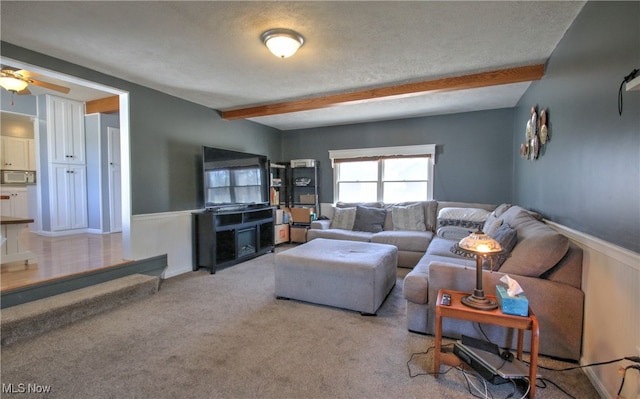 living room with a textured ceiling, beamed ceiling, carpet floors, and ceiling fan