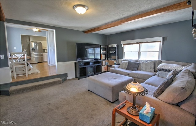 living room with a textured ceiling, carpet, ceiling fan, and beamed ceiling