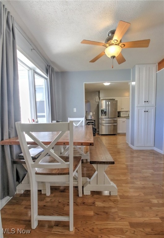 dining area with ceiling fan, hardwood / wood-style flooring, and a textured ceiling